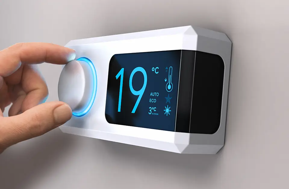 A hand adjusts the dial on a modern digital thermostat mounted on a wall. The screen displays the current temperature of 19°C and options for auto and eco modes, keeping in mind the upcoming Gas Boiler Ban 2035 in the UK, with an outside temperature of 3°C.