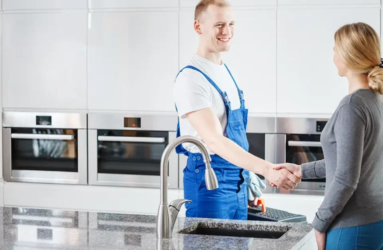 In a modern kitchen, where gleaming built-in ovens catch the eye, two people shake hands by a granite countertop with a shiny faucet. Their warm exchange echoes the importance of asking top questions before hiring a boiler repair company in bustling Stoke-on-Trent.