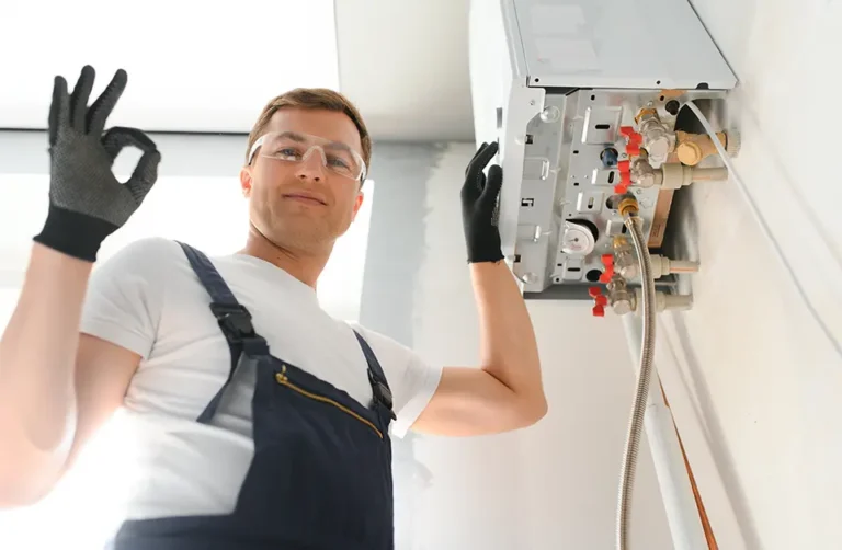 A technician in work gloves stands beside a water heater, giving an "OK" hand gesture, indicating successful installation or maintenance. The image showcases expertise in plumbing services.