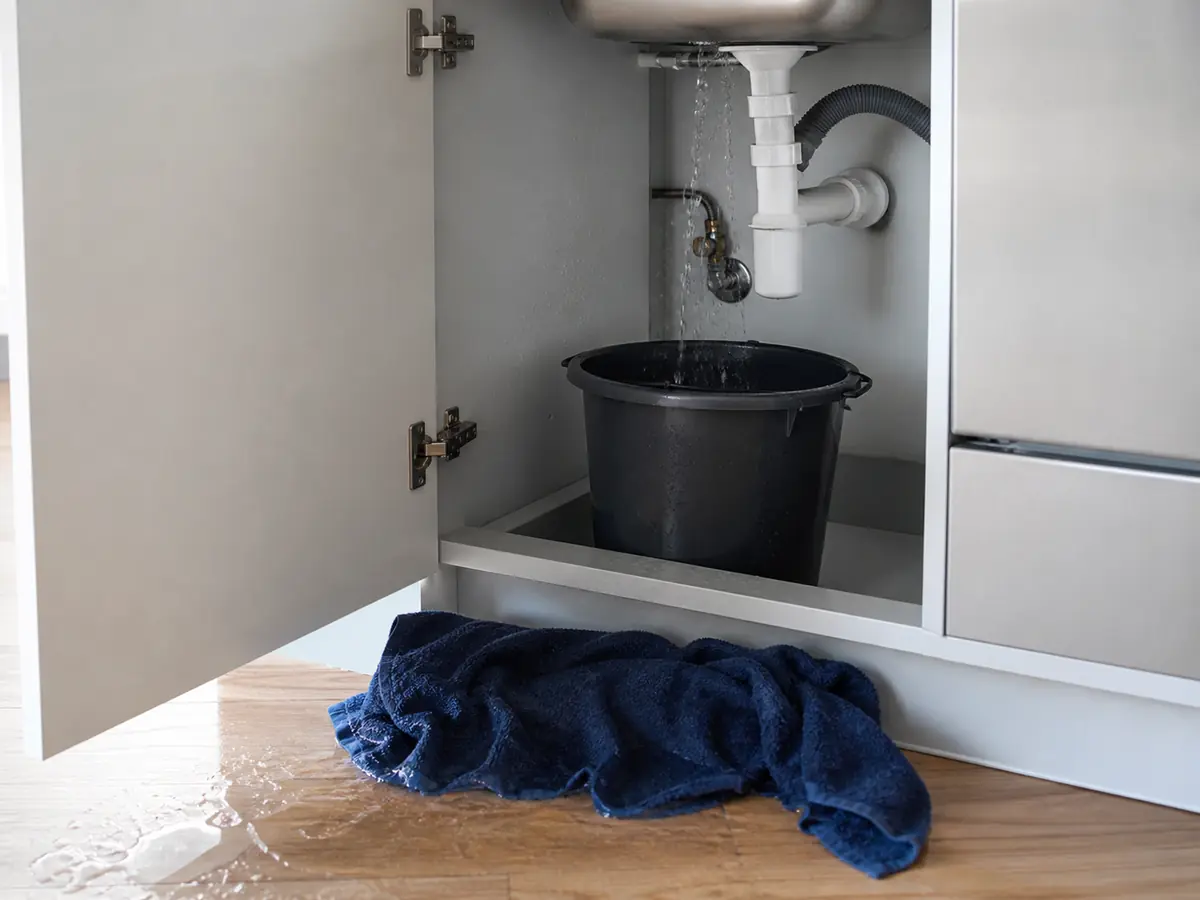 Water leaking from sink pipe into a bucket beneath the cabinet