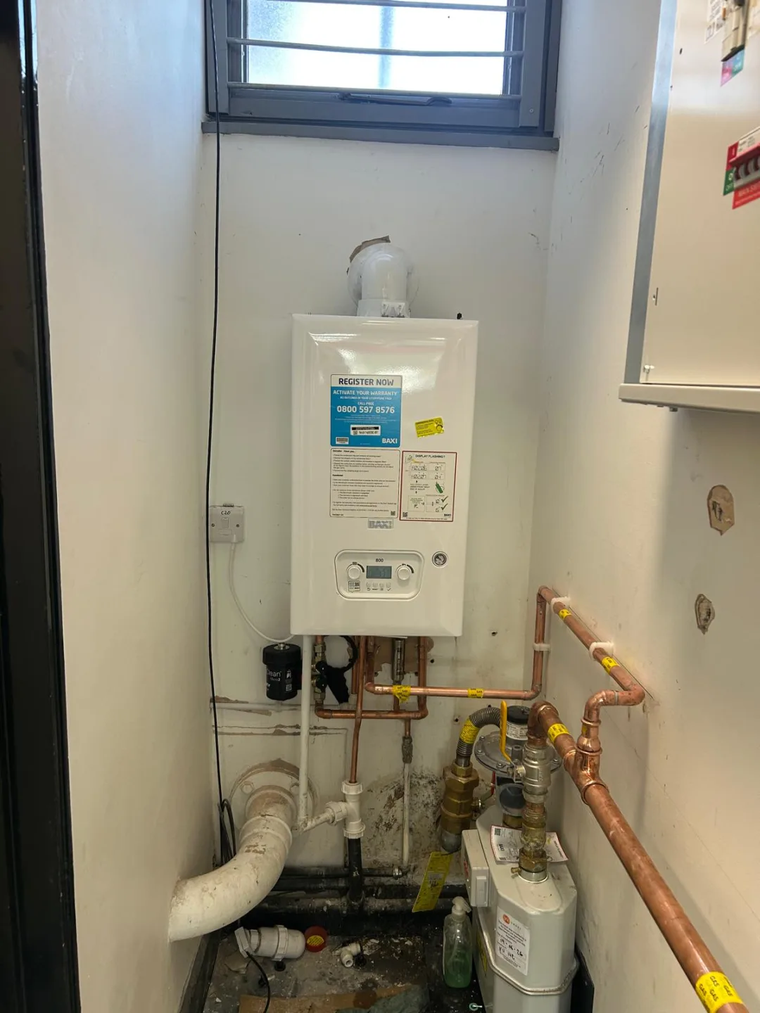 Boiler in a plant cupboard with copper pipework, valves and the gas meter below