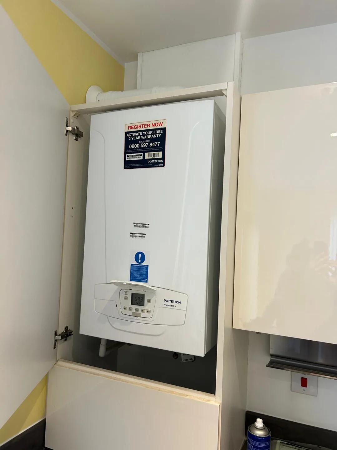 Boiler housed inside a kitchen wall cupboard with the door opened for access