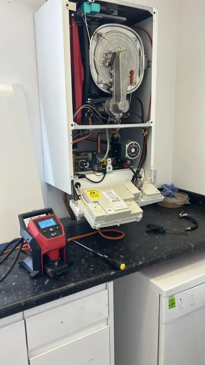 Boiler with its front casing removed on a worktop, heat exchanger exposed and test equipment alongside