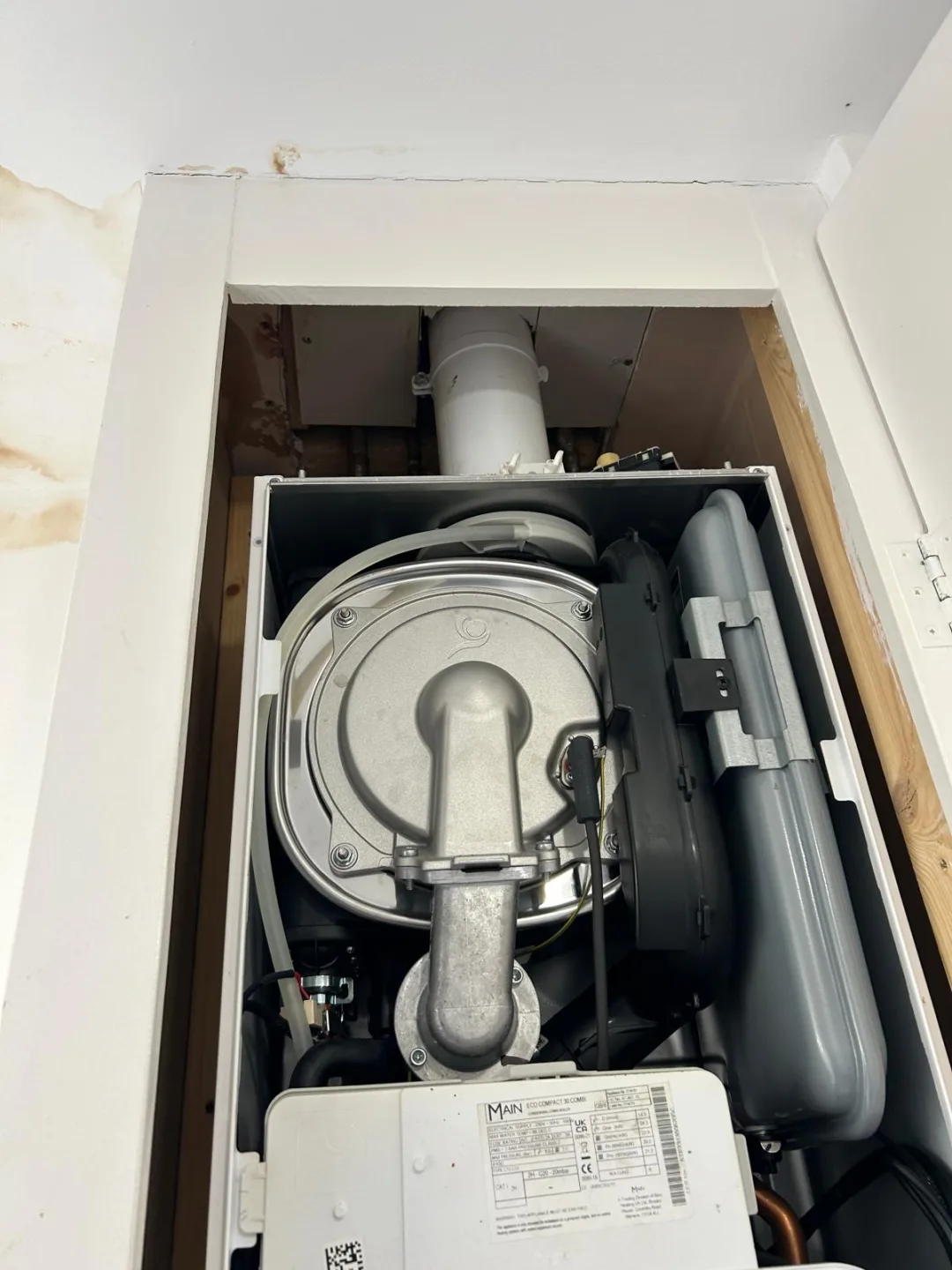 Boiler opened inside a cupboard, flue and fan assembly visible during inspection