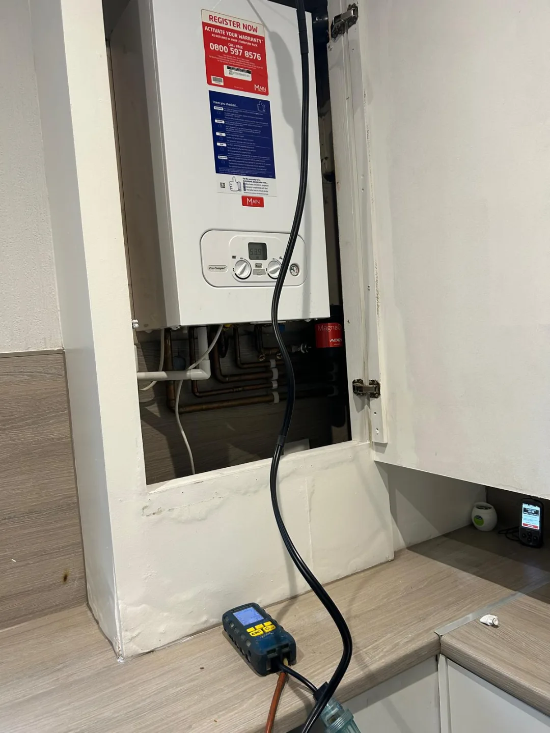 Boiler above kitchen units being tested, analyser hose running down to the floor